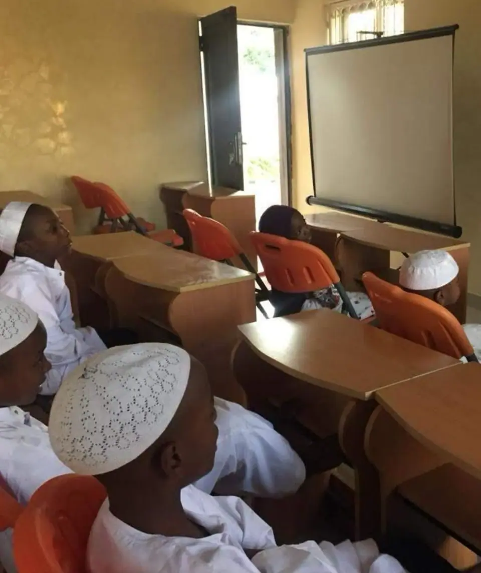 Pupils in white kaftans and caps at their desks beside the classroom window