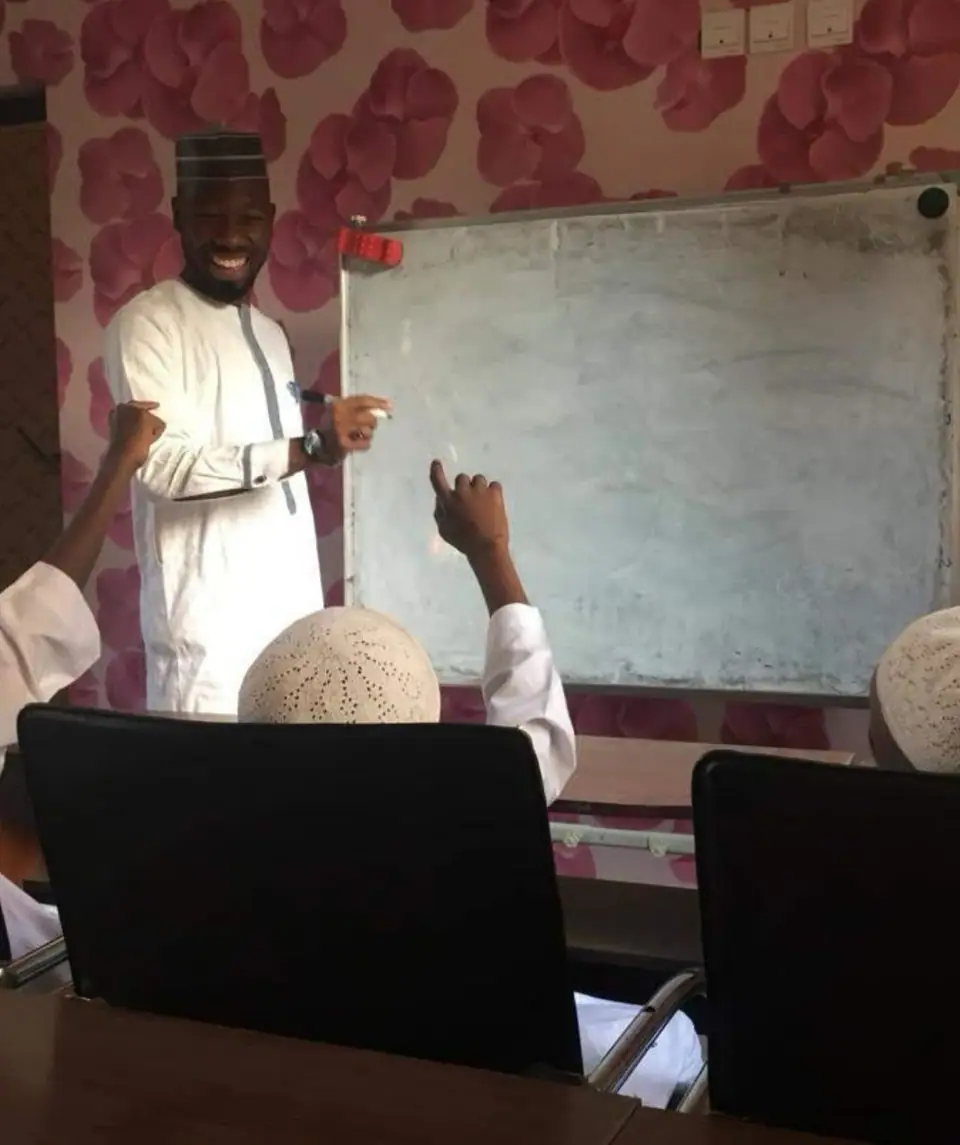 A teacher smiling at the whiteboard as a pupil reaches up to point at what is written on it