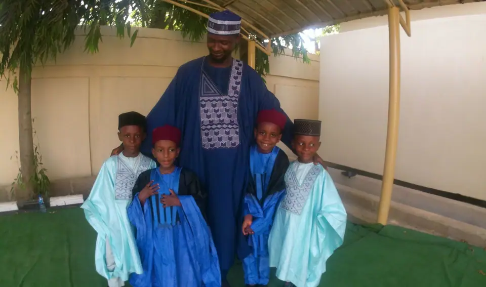 A teacher in a dark blue embroidered robe standing with four pupils in blue and turquoise robes