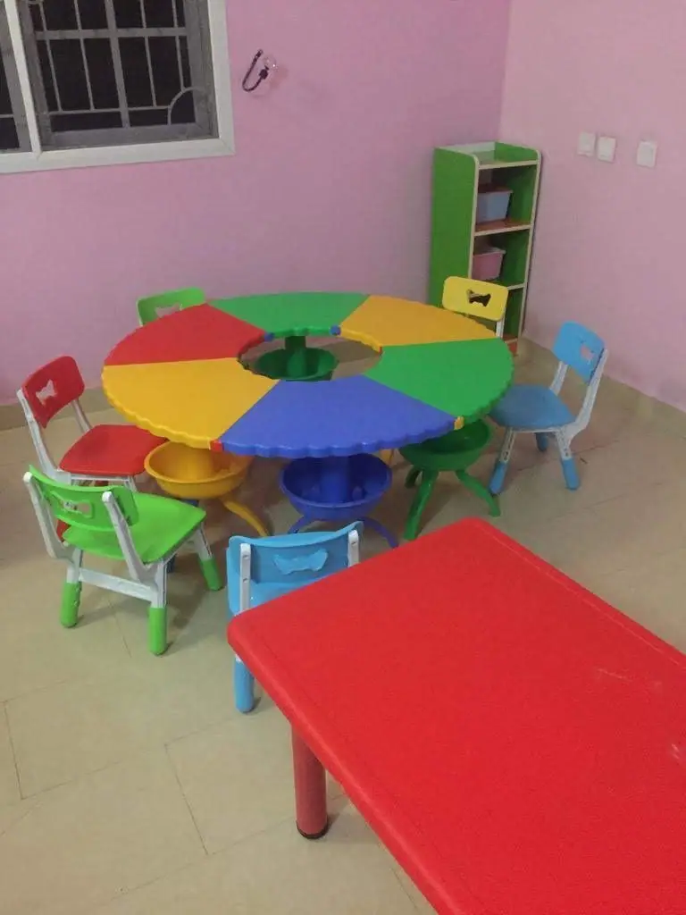The nursery classroom, with a colourful round table, small chairs and a shelf of trays against pink walls